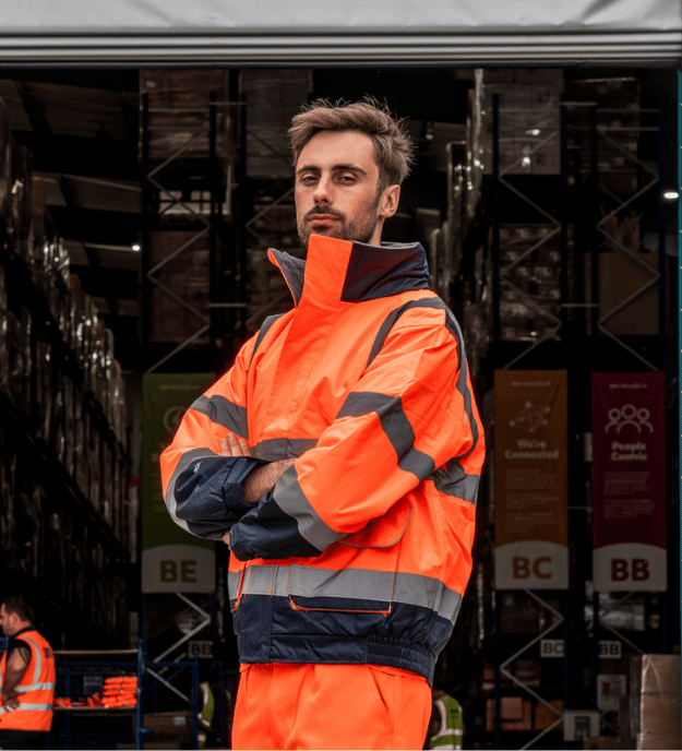 Man in orange hi-vs workwear stood in front of a warehouse.