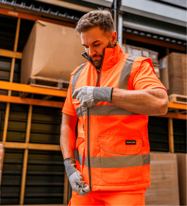 Man in orange hi-vs workwear stood in a warehouse.